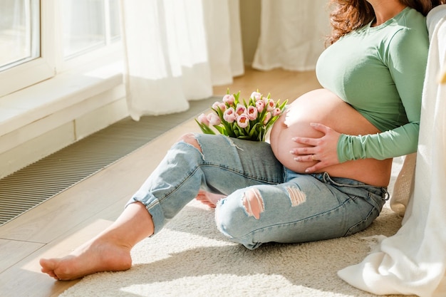 Фото Красивая беременная молодая женщина с большим животом и букетом тюльпанов красочная весенняя беременность