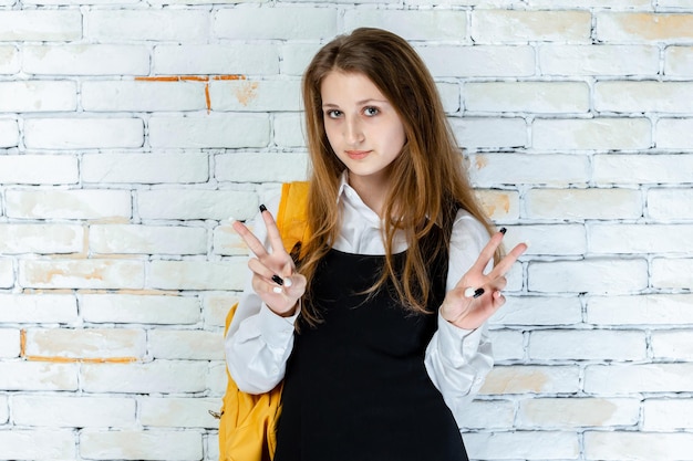 Фото Красивая студентка в форме стоит на белом фоне и жестом мира высокое качество фото