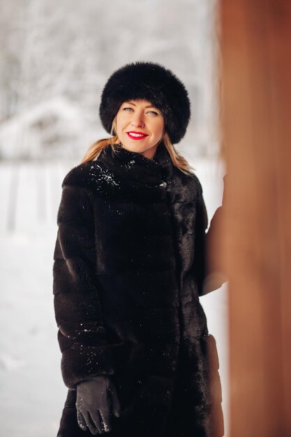 黒い毛皮の帽子と毛皮のコートの肖像画の美しい若い女性かわいいロシアの女の子が微笑んでフレームの赤い唇の明るい化粧を覗き込む