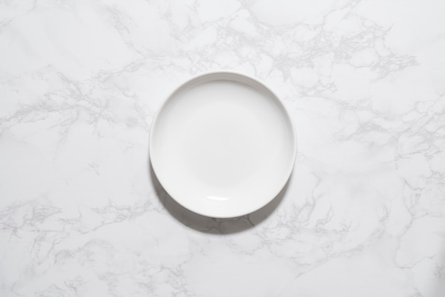 Фото Пустая белая тарелка, помещенная на мраморную тарелку, с высоты птичьего полета