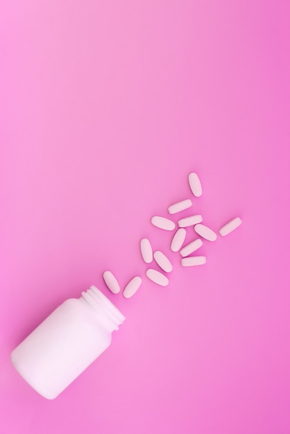 Бутылка с таблетками на розовом фоне. концептуальная медицина. место для текста.