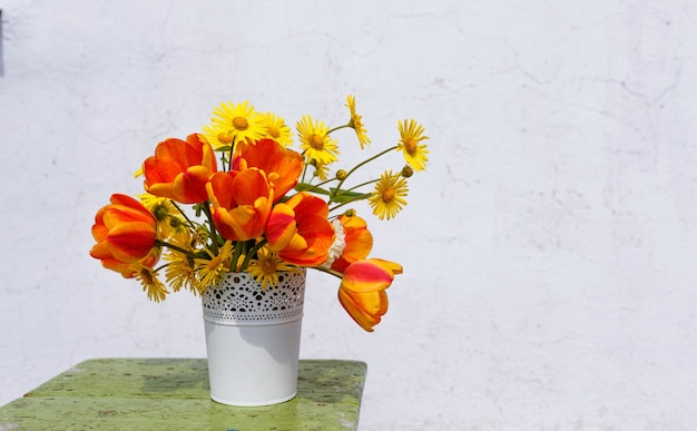 明るい背景に白い花瓶に春の花の花束。木製スタンド。