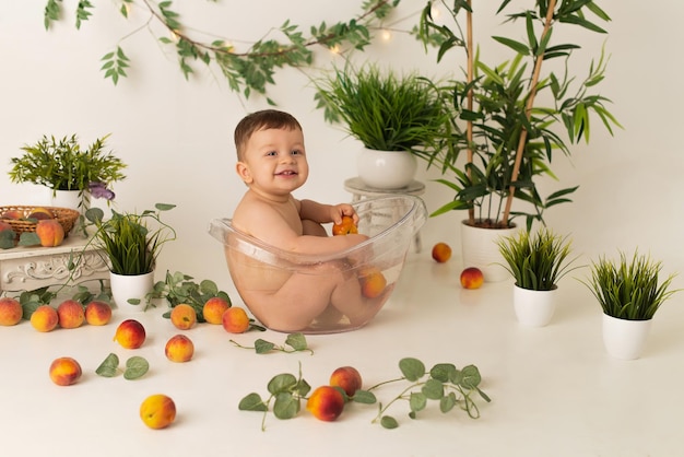 写真 男の子の子供が桃と喜びで白い背景の上のバスルームに座っています。