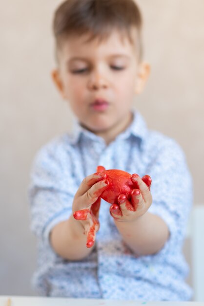 少年は、白い背景にペンキで汚された彼の手で赤いイースターエッグを保持しています。