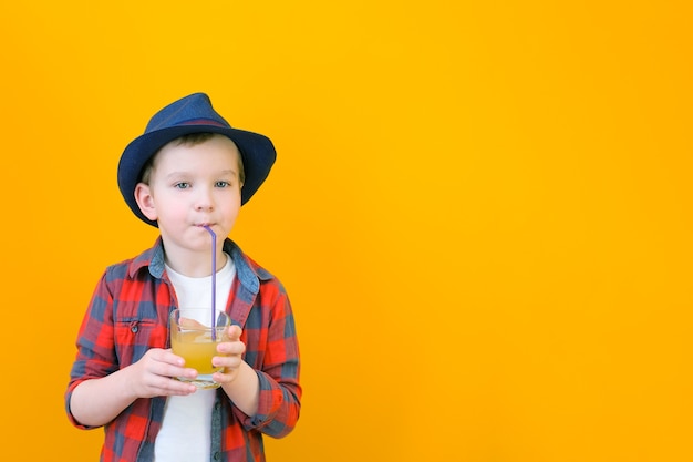 帽子をかぶった少年がストローでジュースを飲みます。リラックスコンセプト。黄色の背景テキストの場所。モックアップ