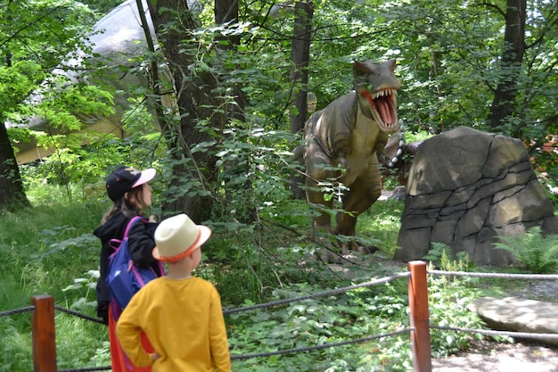 写真 黄色いシャツと白い帽子をかぶった少年が恐竜博物館で恐竜の前に立っています。