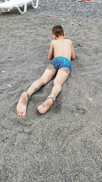 Фото Мальчик в пляжных штанах лежит на скалистом пляже у моря