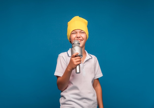 Мальчик поет в микрофон на синем фоне красивый мальчик в белой футболке и шортах стоит на синем фоне и эмоционально поет в микрофон