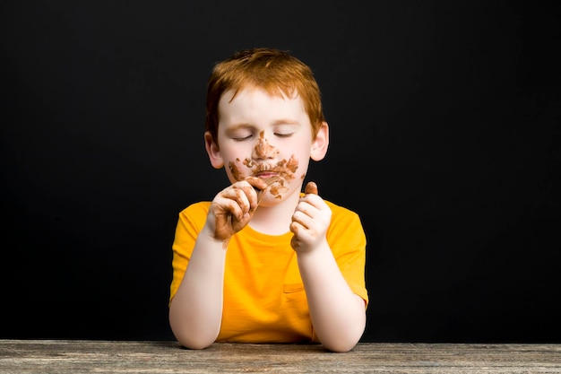 チョコレートで覆われた赤い髪の少年、タイルなどの形をしたミルクチョコレートの汚れた顔と手