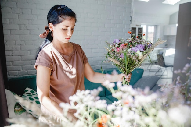 写真 ブルネットのヨーロッパの若い女性の花屋は彼女のワークショップで花とハーブの花束を作ります