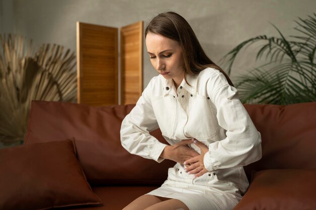 Фото a brunette woman has a stomach ache or menstruation she was sitting on the couch in the living room