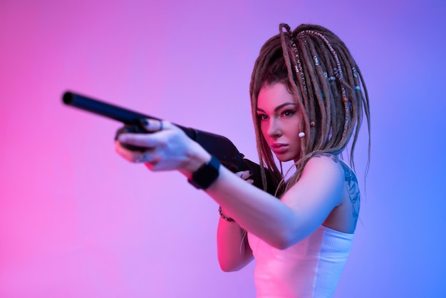 Фото Нахальная девушка с плетенными дредлоками на голове в неоновом свете с пистолетом