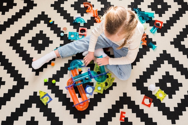 Фото Ребенок играет с магнитным конструктором на ковре дома или в детском саду строим игрушечный домик из кубиков вид сверху