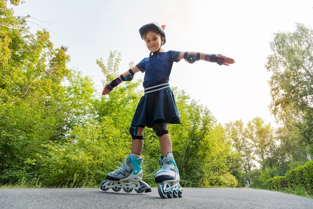 사진 한 어린이가 공원의 녹색 식물을 배경으로 팔을 뻗은 채 롤러 스케이트를 타고 있습니다. 공원에서 롤러 스케이트에 어린 소녀입니다. 균형, 균형, 균형을 잡는 행위