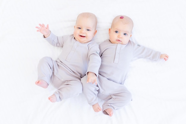 사진 머리에 혈관종이나 종양이 있는 아이 2명의 신생아 쌍둥이 아기가 집에서 하얀 침대에 누워 웃고 있는 면 양복을 입은 소녀