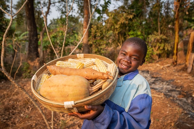 Фото Ребенок, работающий в поле с корзиной урожая, счастливый африканский фермер