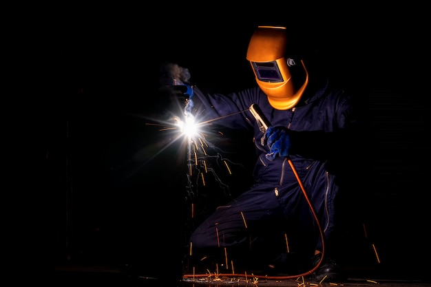 Фото Ремесленник сваривает сталью заготовки. рабочий человек о сварщике стали использование электросварочного аппарата в фабричной промышленности выходят линии света и оборудование для обеспечения безопасности.