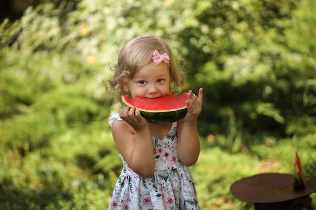 写真 かわいいブロンドの女の子は、高品質の写真の外で夏に新鮮な赤いスイカを食べます