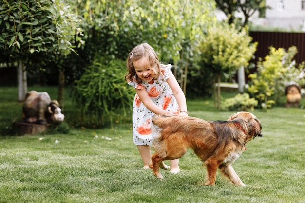 Фото Милая маленькая девочка играет со своей собакой на улице дома на траве.