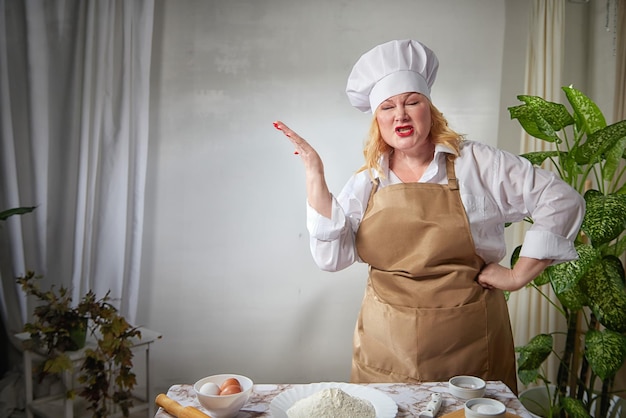 写真 チョコとエプロンを着た太った面白い女性の料理人がキッチンでポーズをとりセルフィーを撮ります