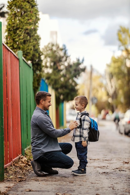 写真 幼稚園に向かう途中父親が息子のボタンを締めています