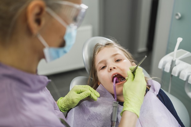 Фото Женщина-дантист осматривает зубы милой маленькой девочки во время стоматологической процедуры в кабинете дантиста.