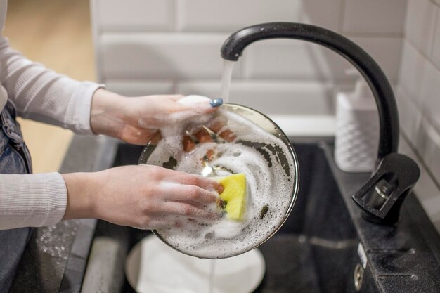 사진 부엌에서 비누 거품 스폰지를 들고 더러운 접시를 씻는 여성 손