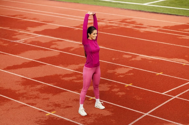 Фото Фитнес-спортсменка растягивает руки и готовится к бегу на стадионе