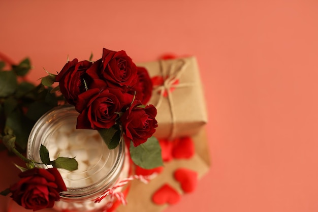 Фото Подарок в крафт-бумаге на розовом фоне в окружении красных роз 14 февраля.