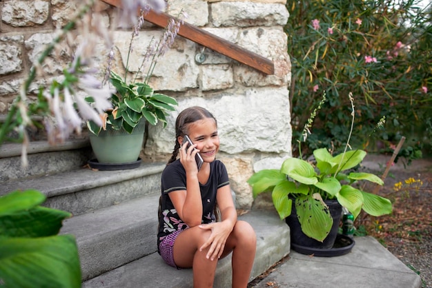 Фото Девушка разговаривает по телефону, сидя на каменных ступеньках в окружении пышной зелени и горшечных растений