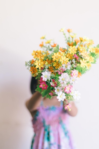 사진 한 소녀가 흰 벽 앞에서 꽃다발을 들고 있습니다.