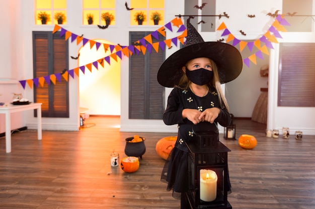 写真 仮面をかぶったハロウィンコスチュームの女の子が秋のお祭りでキャンドルとランタンを持っています