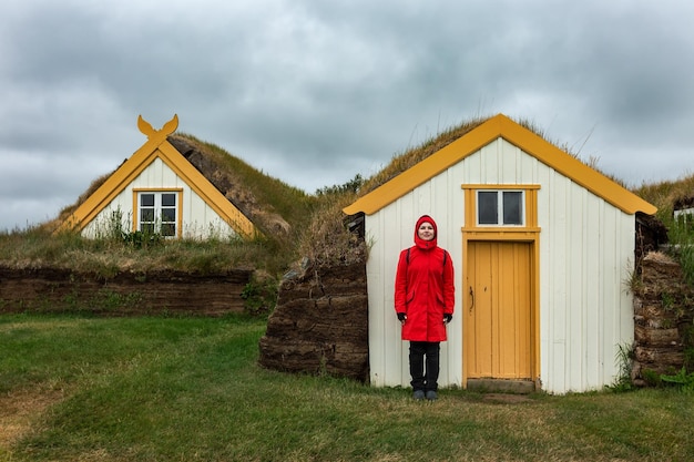 写真 赤いジャケットを着た少女がアイスランドの泥炭の家の近くに立っています.glaumbaer