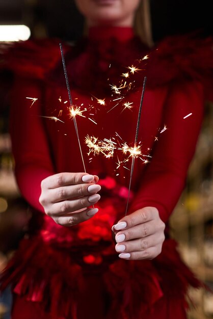 写真 エレガントな赤いドレスを着た女の子が手に線香花火を持っている