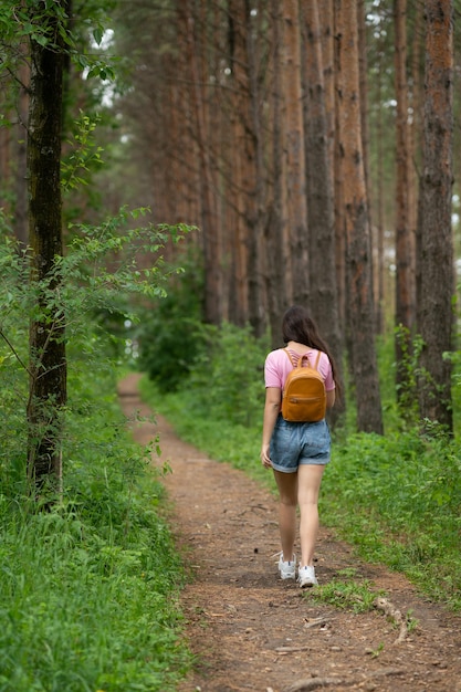 Фото Девушка с рюкзаком за плечами идет по лесной тропинке
