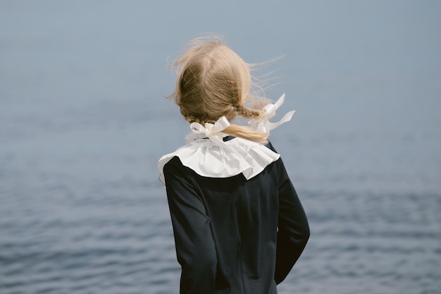 Фото Девочка с косичками стоит спиной в старом школьном платье школьница в синем платье с белым воротником дети у воды