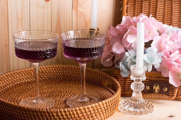 Фото Стеклянный сливочный крем для напитков с цветными напитками алкогольный фруктовый коктейль в плетеной корзине на деревянном фоне с плетеным чемоданом концепция релаксации