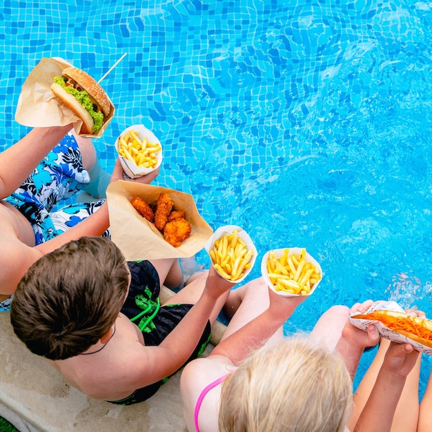 写真 プールのそばに座って、ホットドッグやフライドポテトを食べている子供たちのグループ。