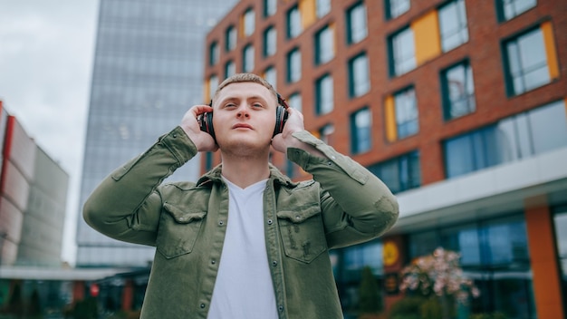 Фото Парень с наушниками ходит и наслаждается прекрасным городским горизонтом перед ним ритм в городе красивый мужчина слушает музыку с наушницами