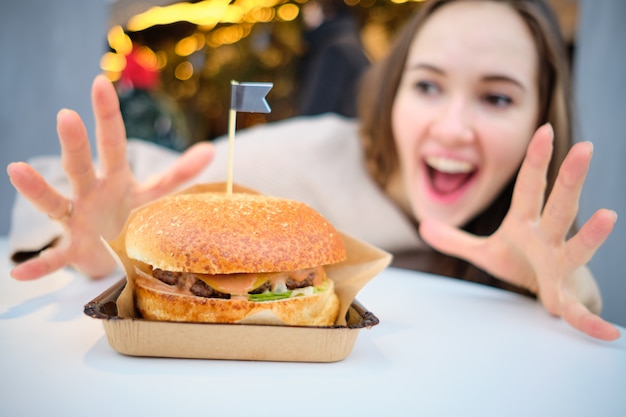 Фото Гамбургер на столе перед девушкой, которая показывает своими руками вау.