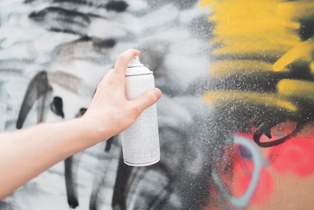 Фото Рука, держащая баллончик с краской, художник рисует граффити на стене