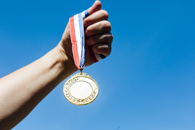 Фото Рука держит золотую медаль за первое место на фоне неба. концепция победы