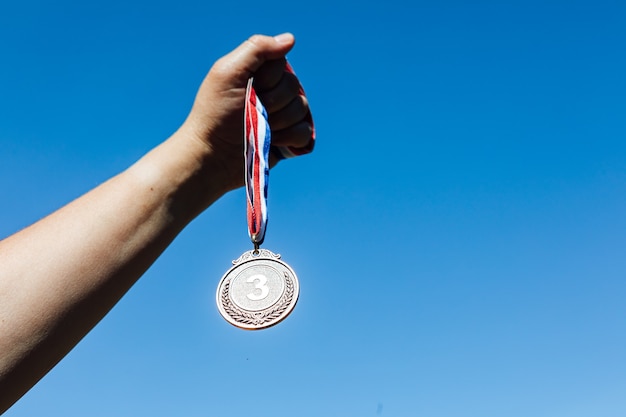 写真 空を背景に、手が3位の銅メダルを掲げています。勝利の概念