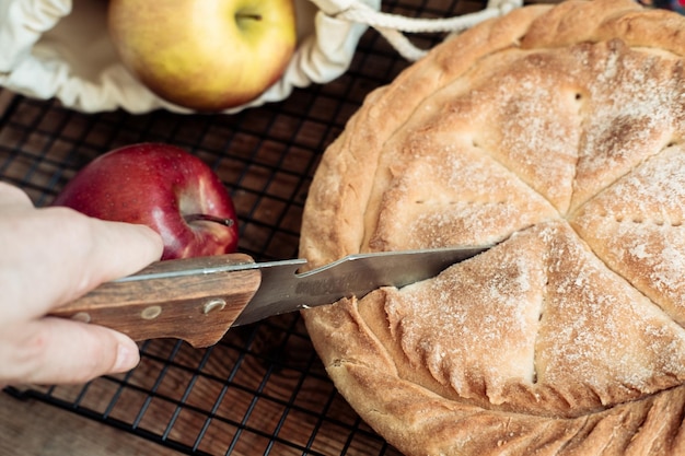 Фото Рука с ножом режет круглый яблочный пирог на деревянном фоне вид сбоку