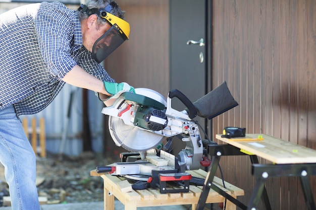 写真 保護用ヘルメットをかぶった便利屋がマイターソーで作業します