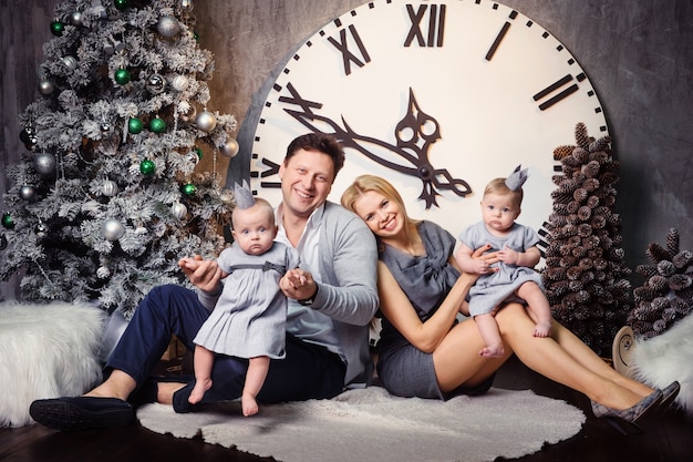 Фото Счастливая большая семья с детьми-близнецами в новогоднем интерьере дома на фоне больших часов.
