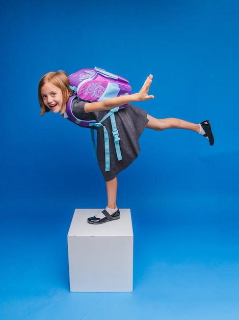 Счастливая маленькая школьница стоит на белом кубе на синем фоне