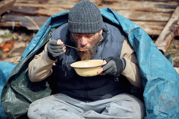 ホームレスの男性が廃墟の近くの皿からスープを食べ、伝染病の最中に貧困層と飢えた人々を助ける