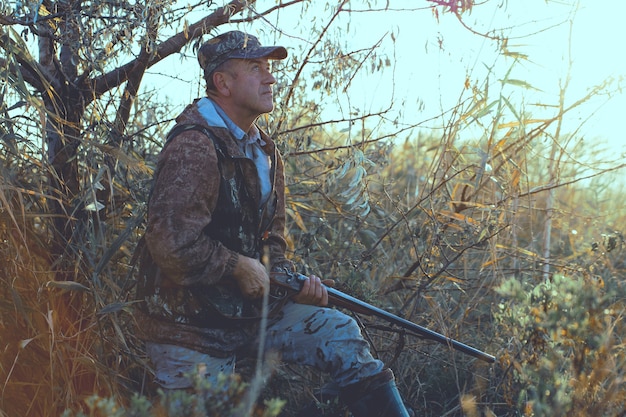 Фото Охотник с ружьем в руках в охотничьей одежде в осеннем лесу в поисках трофея