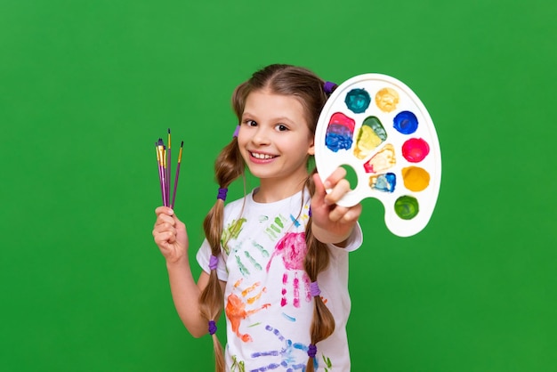 Фото Маленький художник с разноцветной палитрой красок и кистей для рисования на зеленом изолированном фоне курсы искусства для школьников